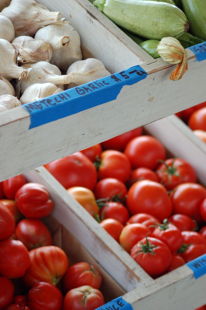 Close-up of fresh garlic, tomatoes, and zucchinis at a local farmers market.